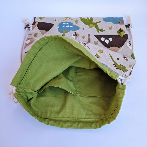 Open Baby dinosaur drawstring backpack with green lining and two internal pockets and natural drawcords