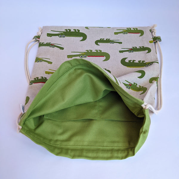 Open crocodile drawstring bag showing internal pockets, green lining and natural drawcords